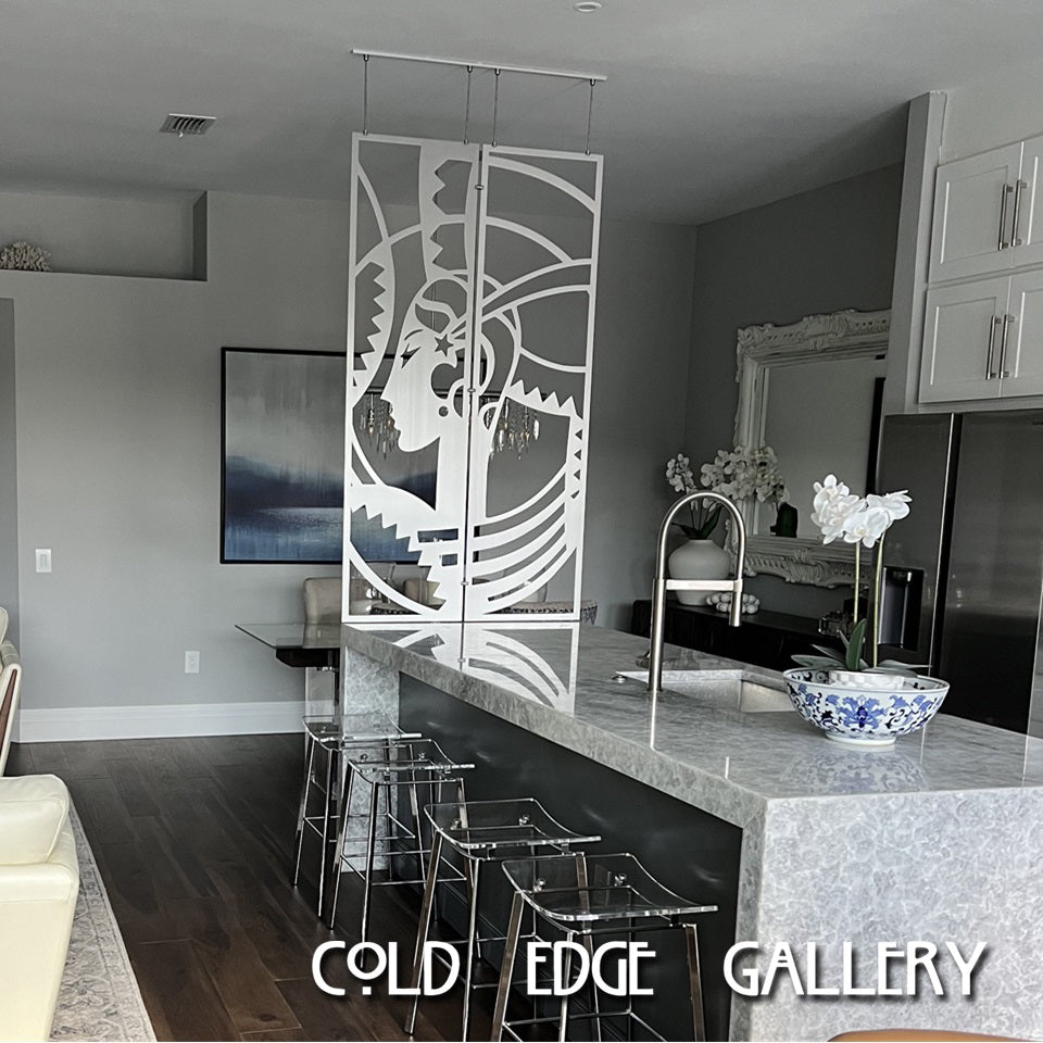 A modern kitchen with a marble island and a custom decorative room divider hanging above, featuring an abstract geometric design by Cold Edge Gallery. Transparent bar stools line the island.