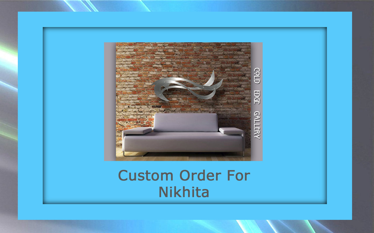 A modern gray sofa is placed against a brick wall with sleek, abstract metallic artwork above it. The text reads "Custom Order For Nikhita" with "Cold Edge Gallery" on the side.