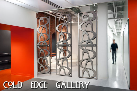 A person walking by a modern indoor space featuring custom metal partitions with curved patterns and the text "Cold Edge Gallery" on the lower part of the image.