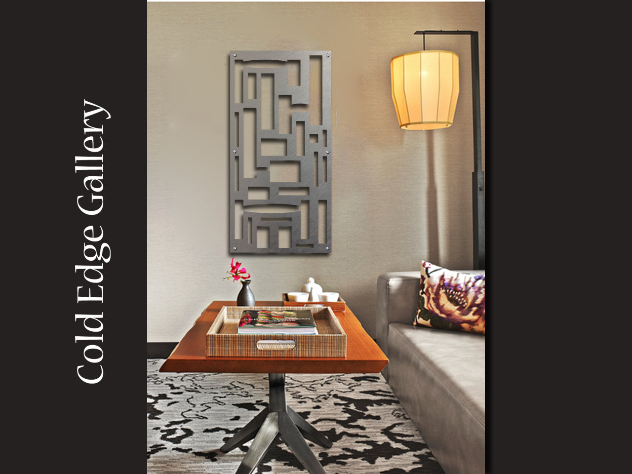 A modern living room with abstract wall art above a custom wooden table. The table holds a tray with a flower and book. A metal lamp hangs near a gray sofa and a patterned cushion. Text reads "Cold Edge Gallery.