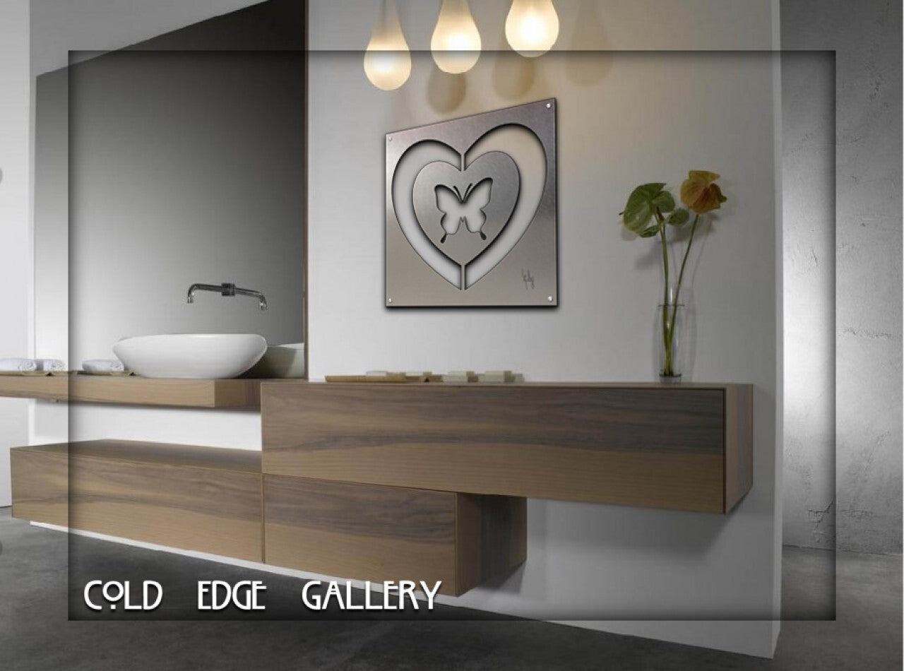 A modern bathroom features a wooden floating vanity with a white sink. Above it, a square artwork with a heart and butterfly design hangs on the wall. Three pendant lights illuminate the space.