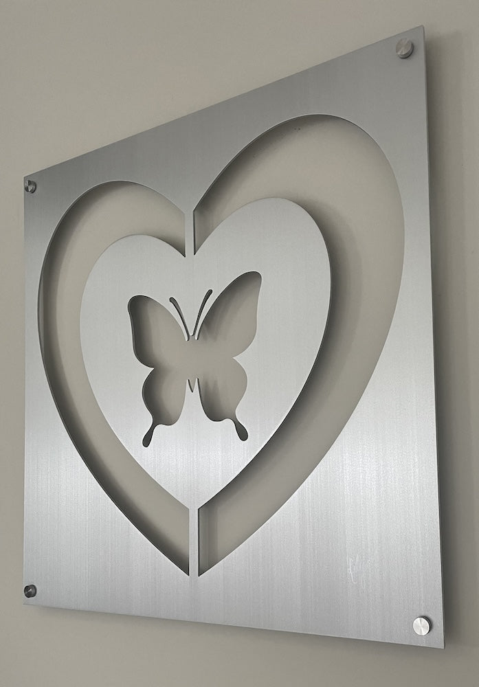 A metallic wall decoration featuring a cut-out design of a heart with a butterfly in the center.