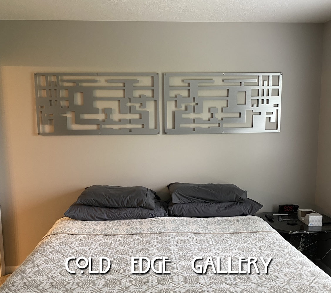 A neatly made bed with two dark pillows and a patterned duvet cover. Above the bed are two geometric metal wall art pieces. "Cold Edge Gallery" text is overlaid on the image at the bottom.