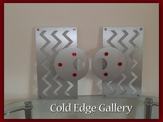 Two abstract metal art pieces with zigzag patterns and circular discs featuring red accents. Below, text reads "Cold Edge Gallery.