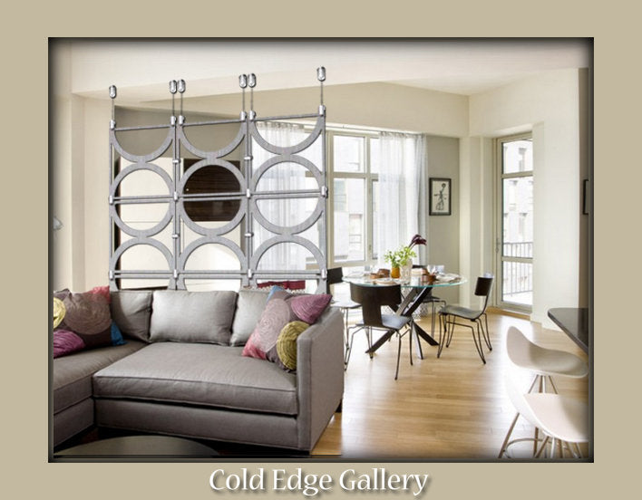 Modern living room with a grey sectional sofa, colorful pillows, and a decorative metal room divider. Dining area with a round table and chairs in the background. "Cold Edge Gallery" text at the bottom.