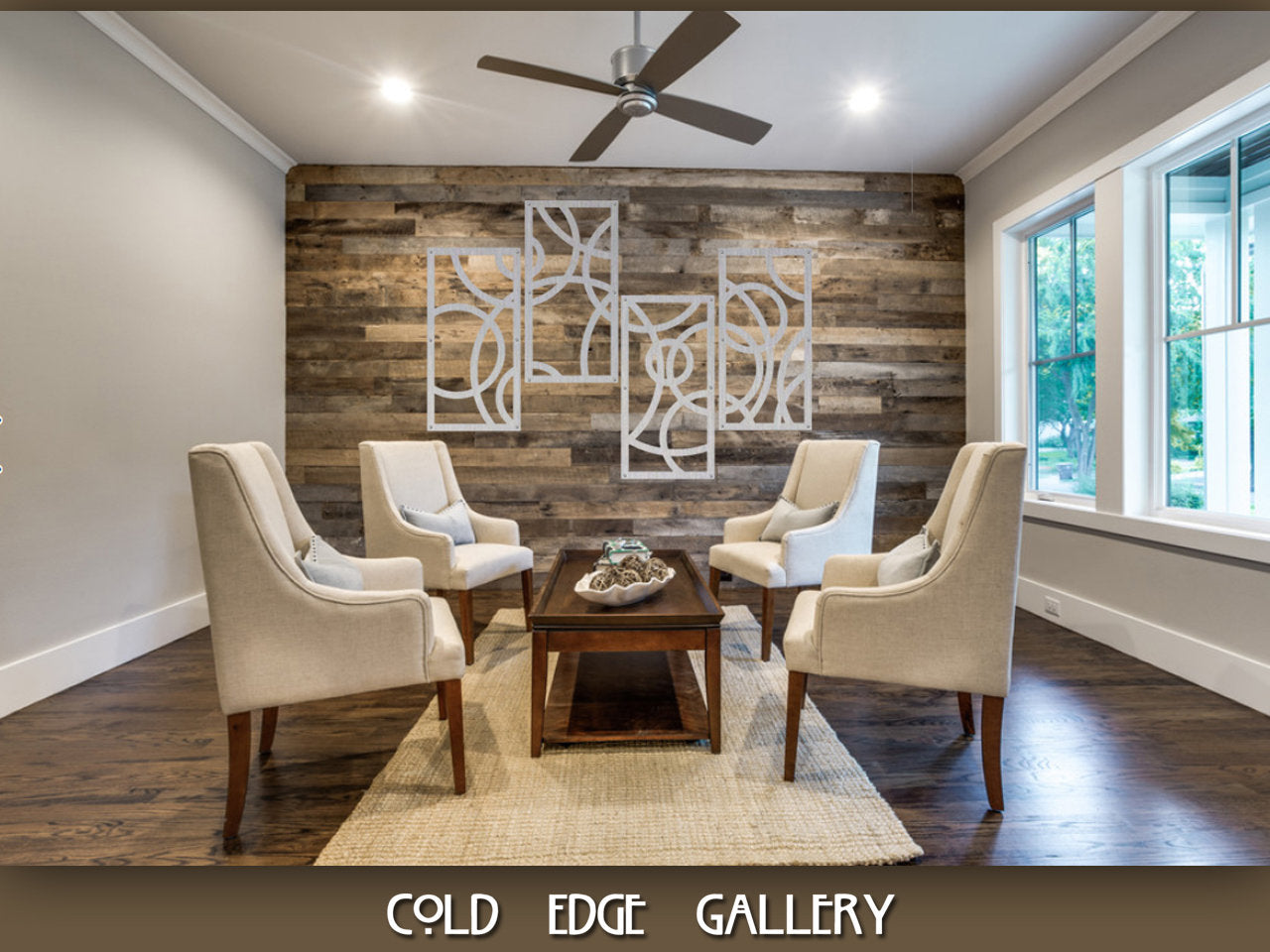 A modern, indoor seating area with four beige chairs, a small wooden coffee table, and geometric wall art on wood-paneled wall. The room has a ceiling fan and large windows. Text "COLD EDGE GALLERY".