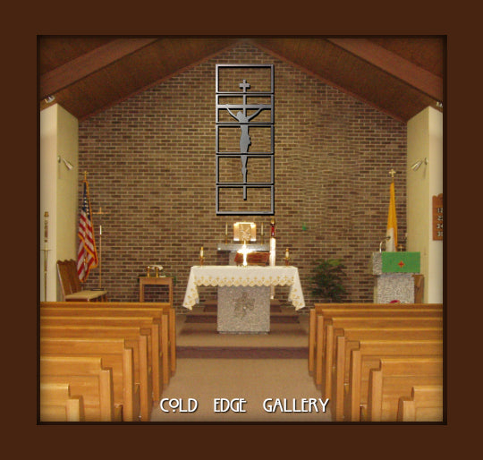 Interior of a chapel with wooden pews facing an altar. A crucifix is mounted on a brick wall behind the altar, which is draped in a white cloth. American and yellow flags are displayed on the left.