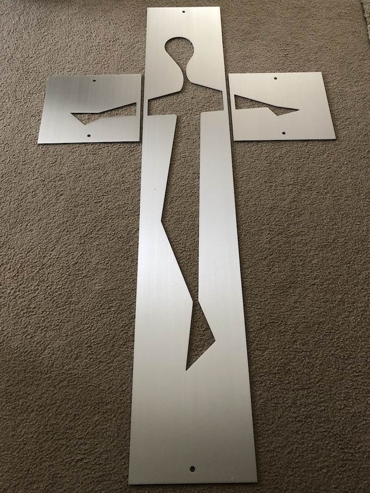 A silver metallic sheet with cutouts depicting a figure resembling a crucifixion, laid flat on a beige carpet.