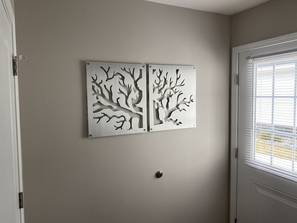 Metal artwork of tree branches displayed on a beige wall near a door with a window.