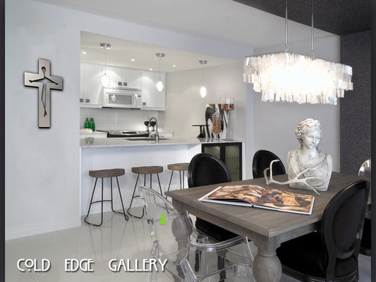 A modern kitchen-dining area with a breakfast bar, stools, and a contemporary chandelier. A bust and an open book are on the dining table. The wall features a cross and the text "COLD EDGE GALLERY.